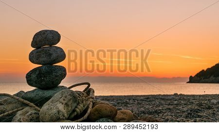 Beach Stone Fireplace With Rope At Sunrise. Sea Water With Rocks In The Background. Vlychada Beach P