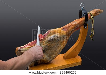 Hand Cuts With Knife At A Spanish Serrano Ham In A Wood - Holder - Isolated