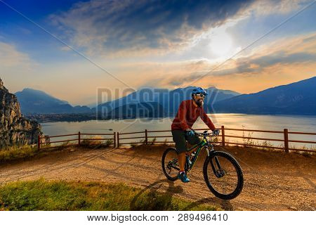 Cycling man riding on bike at sunrise mountains and Garda lake landscape. Cycling MTB enduro flow sentiero ponale trail track. Outdoor sport activity.