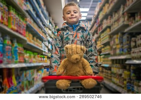 Cute Little Caucasian Boy Shopping With His Teddy Bear In A Basket