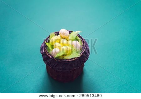 Easter Composition With Traditional Decor. Small Colorful Eggs And Feathers In Wicker Basket On Soft