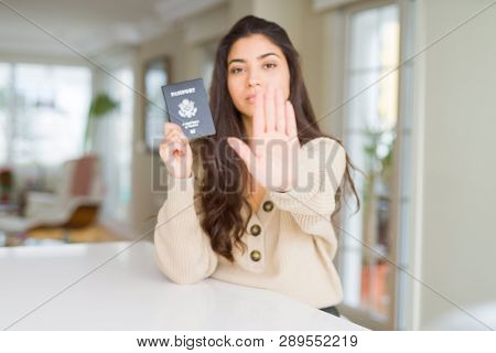 Young woman holding passport of United States of America with open hand doing stop sign with serious and confident expression, defense gesture