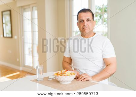 Middle age man eating rice at home with serious expression on face. Simple and natural looking at the camera.