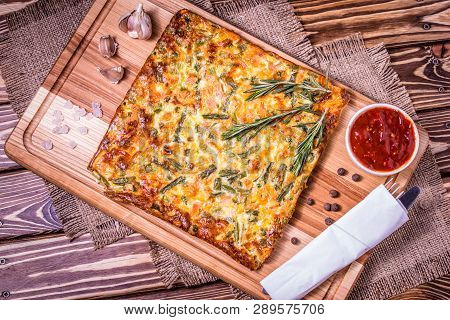 Spanish Omelet With Vegetables On A Board With Sauce, Salt And Pepper On A Wooden Table With A Spoon