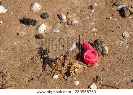 Damaged Red Wistle For Kids, Forgotten Or Lost On The Sand Of A Beach, Among Stones And Shells. Part