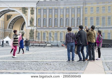 A Woman Tourist Of Eastern Appearance Posing For A Group Of Compatriots On The Palace Square Of St. 