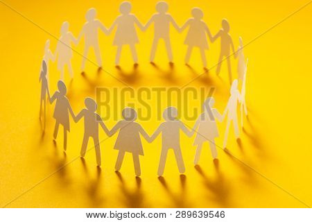 Circle of paper people holding hands on yellow surface. Community, union concept. Society and support.