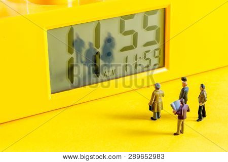 Yellow Alarm Clock With At Eleventh Hour Time With Little Miniature Figurines Standing In Front Of T