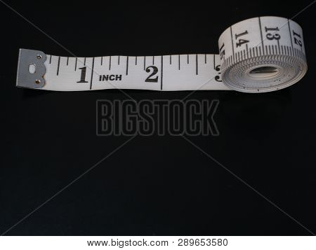 Rolled Measure Tape With Inches Numbers On Dark Black Background And Lot Of Copy Space. Can Be Easil