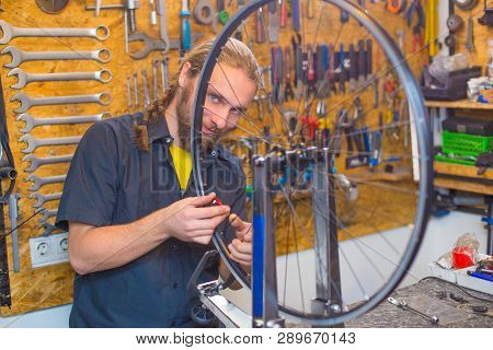 Blue Eyed Beraded Guy In Black Shirt Repairing Bicycle In The Workshop