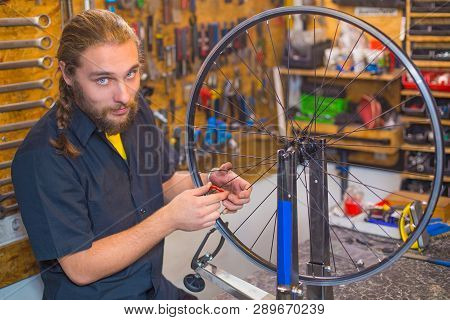 Blue Eyed Beraded Guy In Black Shirt Repairing Bicycle In The Workshop
