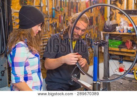 Handsome Beraded Guy And The Pretty Girl Repairing Bicycle In The Workshop Together