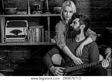 Lady And Man With Beard On Dreamy Faces Hugs And Plays Guitar. Couple In Wooden Vintage Interior Enj