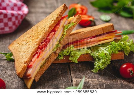 Sandwich With Ham, Cheese, Tomatoes And Lettuce Leaves On Wooden Rustic Table. Close Up