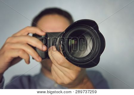Young Man Using A Professional Camera. Close Up Photo Of Man In Hat On Blue Background Taking A Phot