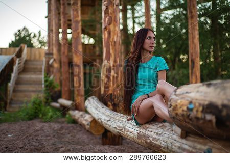 Girl In Turquoise Short Dress Sitting On A Tree Log