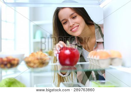 Portrait Of Female Standing Near Open Fridge Full Of Healthy Food, Vegetables And Fruits. Portrait O