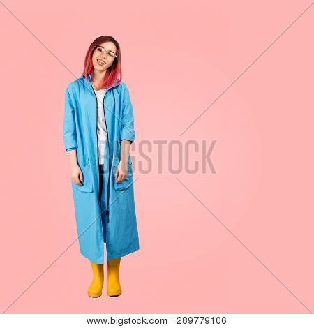Studio Shot Of A Full-length Young Girl In A Blue Coat And Yellow Rubber Boots With A Funny And Comi