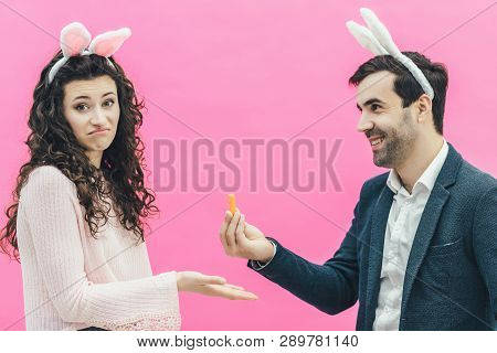 Young Happy Couple On The Pink Background. On The Head Is A Rabbit Ears. A Young Man Holding A Small
