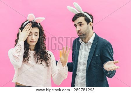 Young Happy Couple On The Pink Background. On The Head Is A Rabbit Ears. A Young Girl Holding A Carr