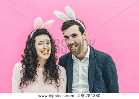 Young Happy Couple Standing On Pink Background. On The Head Of The Ears Of The Bunny. During This Ma