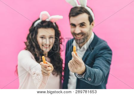 Young Beautiful Couple Standing On A Pink Background. On The Head Of The Ears Of The Bunny. During T