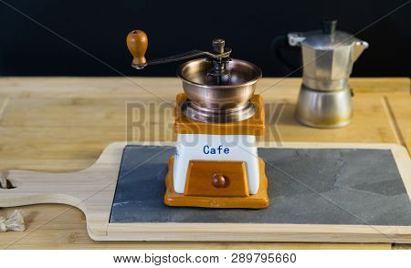 Close-up Of An Old Italian Coffee Grinder That Stands On A Stone Stand, In The Background A Moka And