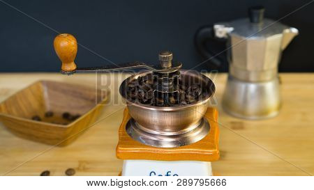 An Old Italian Coffee Grinder Close Up, In Which Is Poured With Roasted Coffee Beans, In The Backgro