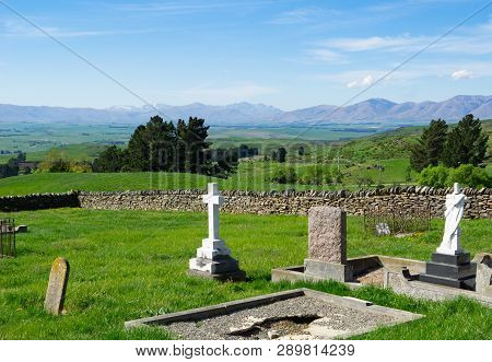View Across Old Cemetery With Broken Headstones To Expansive Rural Fields And Distant Hills In Centr