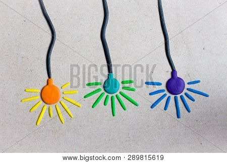 Three Colorful Lamps Of Blue, Violet And Orange Colors Hang On Even Wires Against A Gray Wall. Lamps