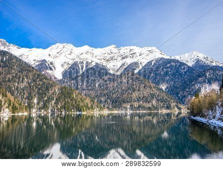 Beautiful Mountain Lake In The Spring. In The Background, Mountains Covered With Snow Are Reflected 