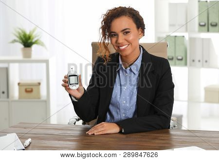 Young African-american Woman With Digital Glucometer At Workplace. Diabetes Control