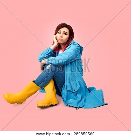 Young Beautiful Girl In A Blue Coat And Yellow Rubber Boots Sits With A Sad Expression In Her Eyes. 