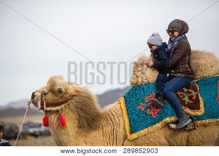 SAGSAY, MONGOLIA - SEP 30, 2017: Local Kazakh woman rides children on a camel during a local holiday. 