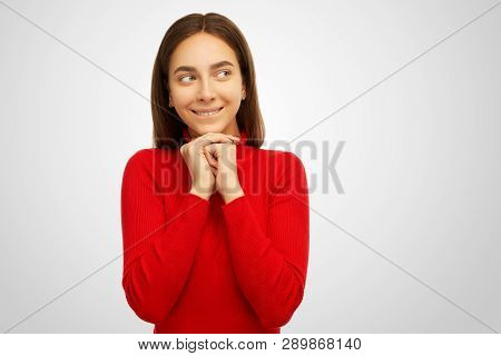 Beautiful Young Joyful Woman Keeps Hands Together, Has Green Eyes Full Of Happiness, Stands Against 