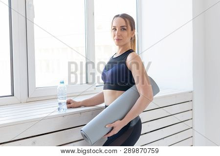 People, Sport And Fitness Concept - Young Woman With Yoga Mat And Bottle Of Water Standing Near Wind