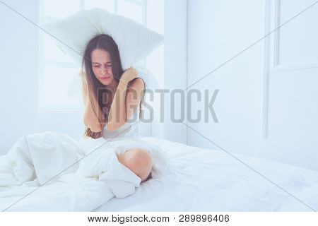 Young caucasian woman covering her head and ears with pillows.
