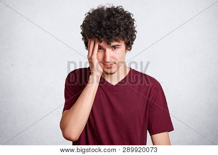 Portrait Of Young Boy With Little Beard And Curly Dark Hair, Keeps Hand On Temple Isolated On White 