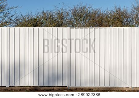 Two Panels Of A White Metal Fence Used To Screen Off A Wooded Site