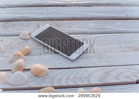 The Smartphone Lies In The Encircling Of Seashells On Wooden Boards.