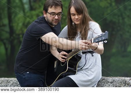 Older Brother Teaching His Younger Sister To Play Guitar In The Nature. Beautiful Moments Spent Toge