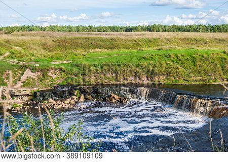 Waterfall, Water Flowing From The River Falls Down. A Stormy River With A Brown Hue.