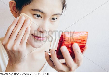 Portrait Of Asian Woman Applying Foundation Powder Puff On Her Face To Cover Flaws And Change The Na