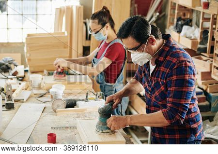 Team Of Carpenters In Protective Masks Polishing Wooden Crates With Orbital Sander Hand Tool