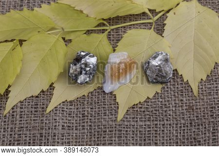 Three Semi-precious Stones, Two Phlogopites And Citrine, Lie On A Jute Fabric On Autumn Yellow Leave
