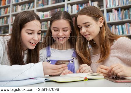Charming Teen Girls Using Smart Phone While Studying At Colege Library. Connection, Online, Social M
