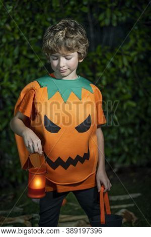 Happy Halloween. Boy Dressed In A Pumpkin Costume With Burning Candle In The Hand On The Night Garde