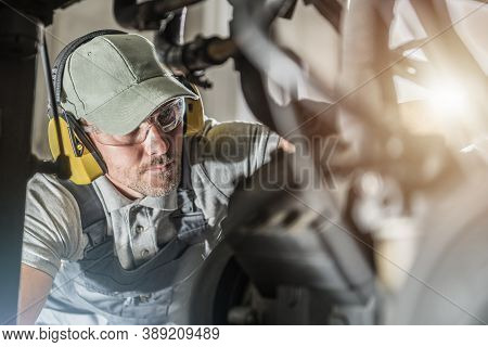 Caucasian Automotive Industry Technician In His 40s Wearing Safety Glasses Looking Into Engine Compa