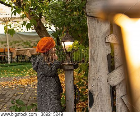 Halloween Autumn Kids. Portrait Magic Girl In Coat, Hat With Street Lantern In Park. Photo