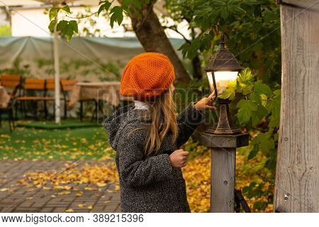 Halloween Autumn Kids. Portrait Magic Girl In Coat, Hat With Street Lantern In Park. Photo